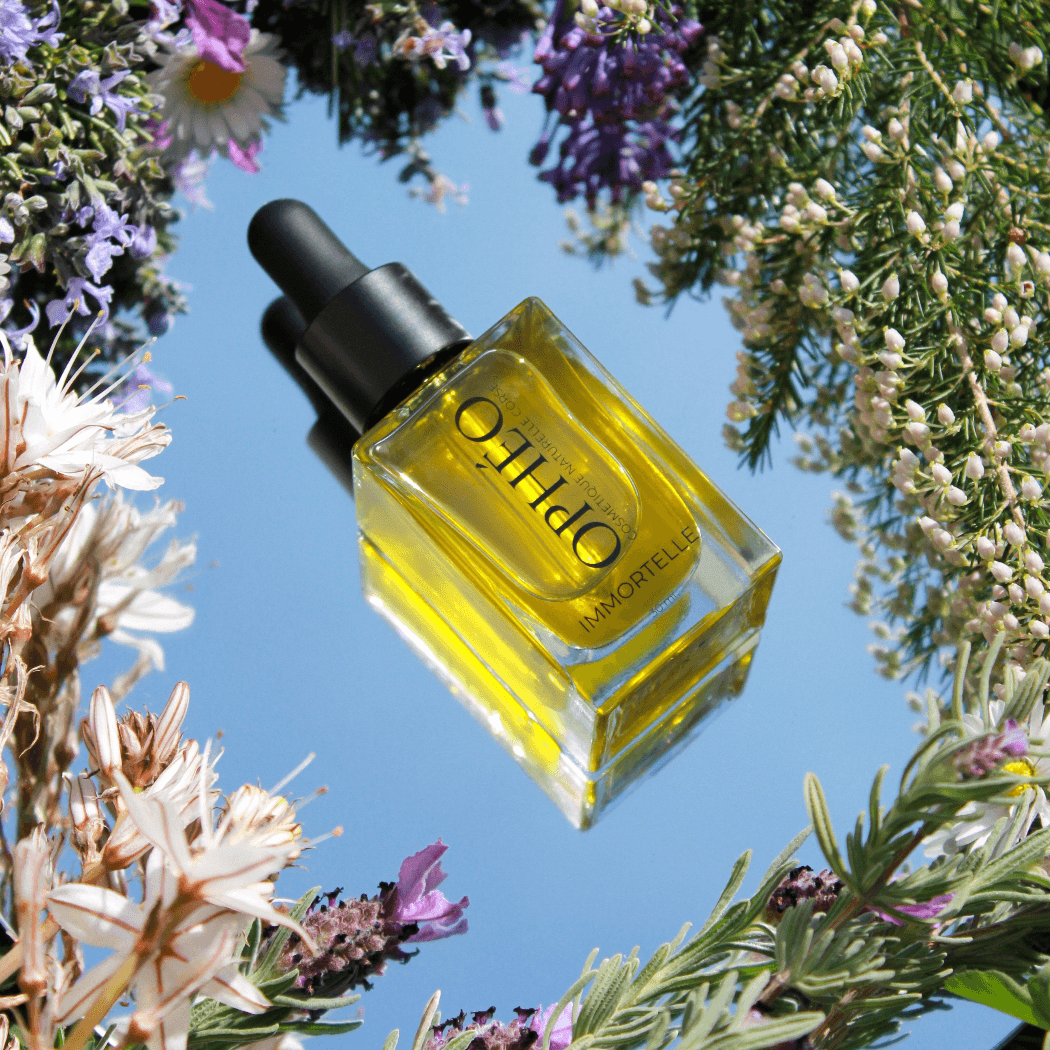 Flacon d'huile visage immortelle OPHÉO, huile immortelle visage pour apporter souplesse et éclat aux peaux ternes, entouré de fleurs de maquis corse.