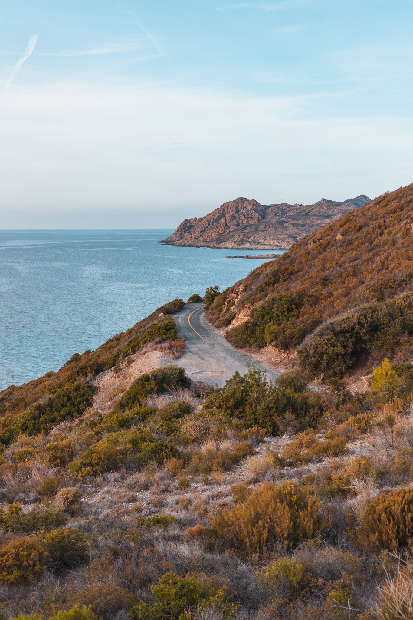 Paysage corse montrant une route au bord de mer, serpentant dans le maquis, à flan de montagne.