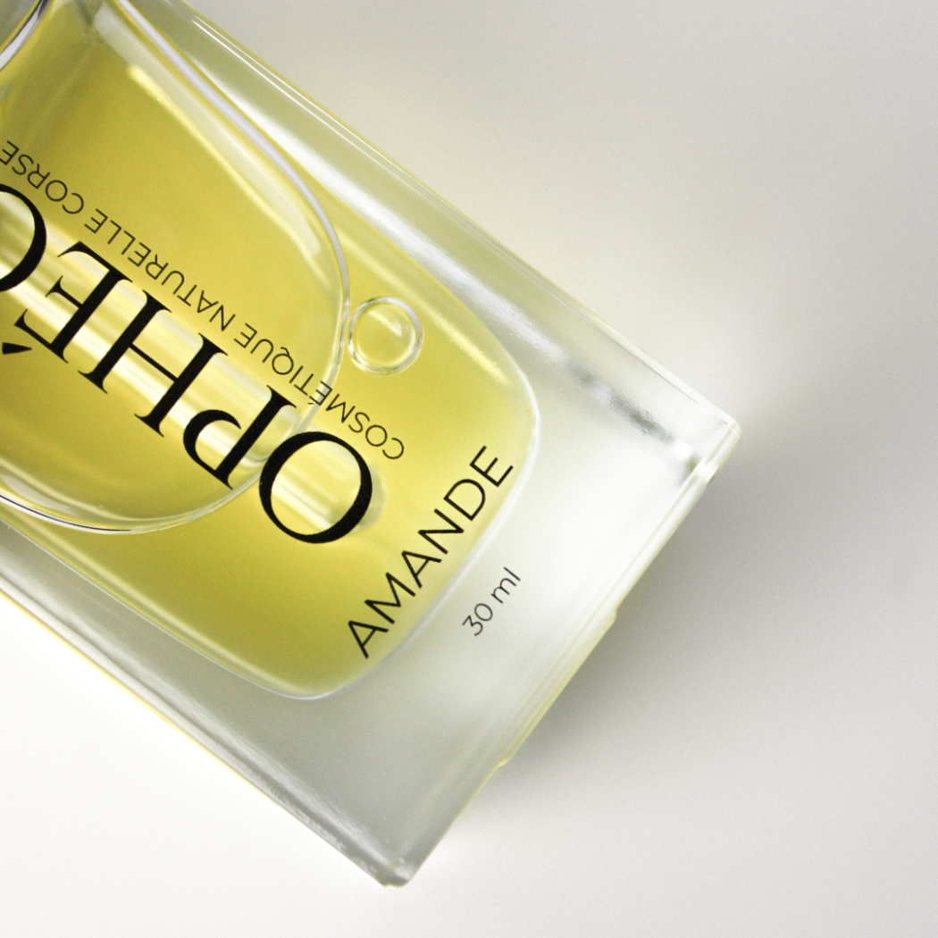 Zoom sur un flacon d'Huile Visage Amande Nourrissante de la marque OPHÉO. On y voit en détail le flacon en verre et l'huile végétale d'amande douce de couleur dorée.